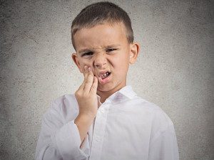 Child in discomfort holding his cheek.